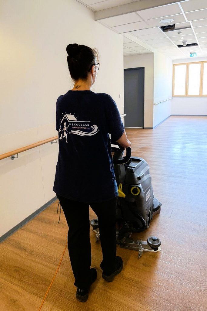 Frau in einem blauen T-Shirt, das einen Bodenreinigungssauger in einem Flur zieht