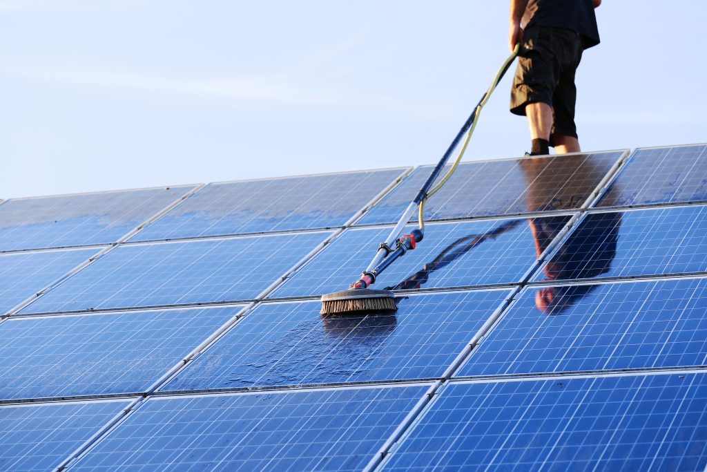 Mann reinigt Solarzellen mit Reinigungsgerät auf Dach